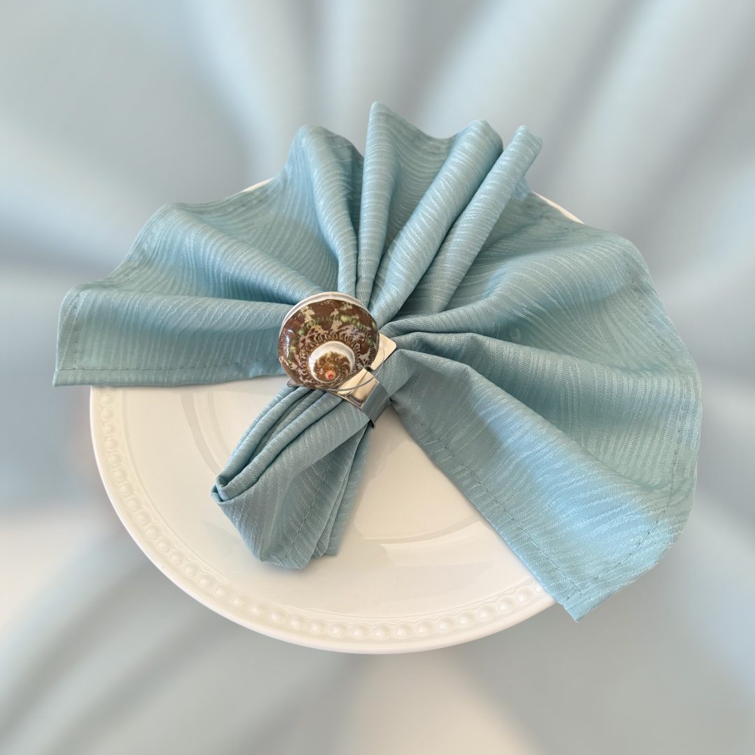 Elegant blue cloth napkin with a shell and pearl napkin ring on a white plate.